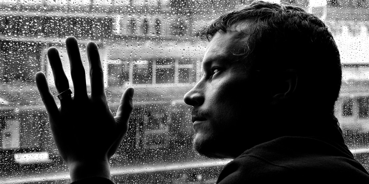 A sad man looking out a window on a rainy day