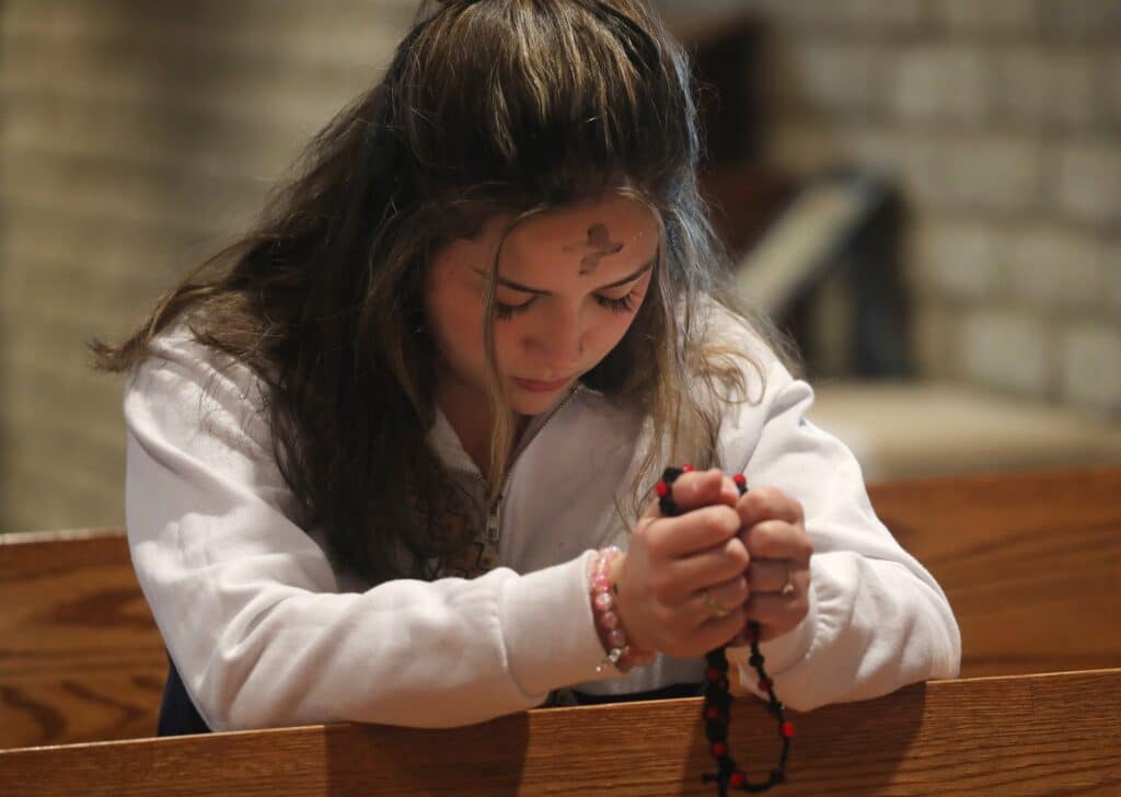 A young woman prays with a rosary following Ash Wednesday Mass at Sacred Heart Church in Prescott, Ariz. (OSV News photo/Bob Roller)