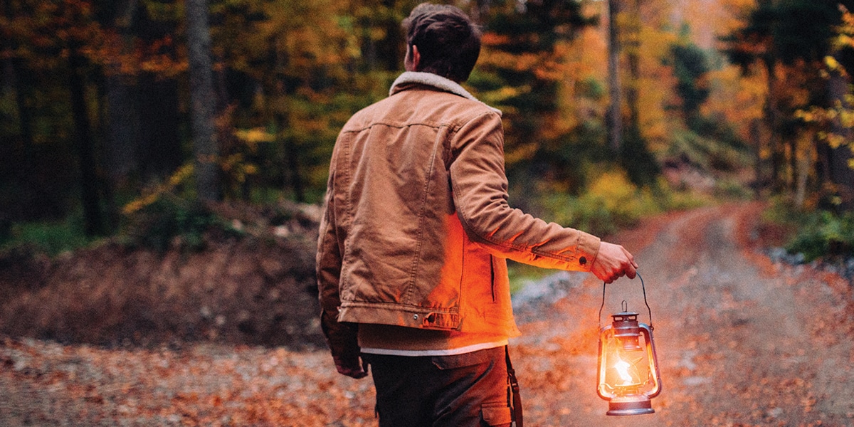 man walking in the woods with a lantern
