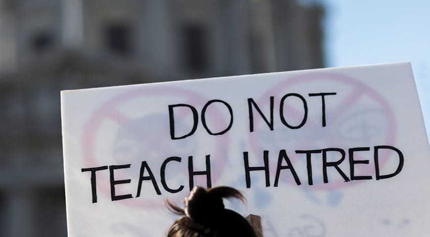 Person holding a sign saying "Do Not Teach Hatred"