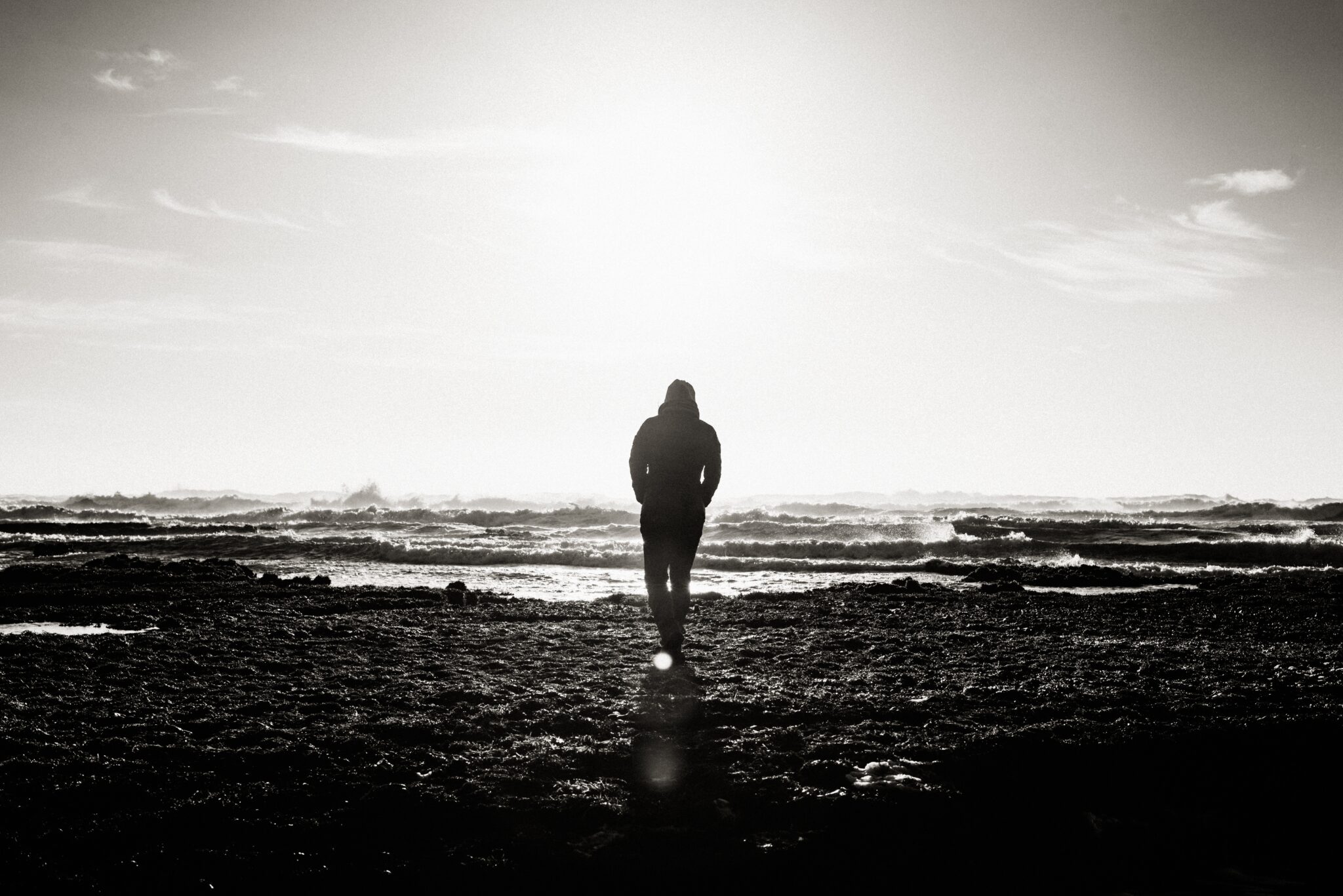 Person walking toward the ocean in black and white