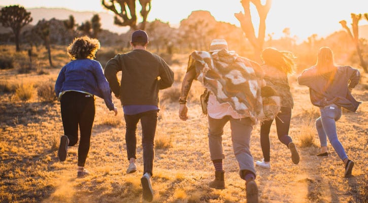 Five friends running through the desert during sunset
