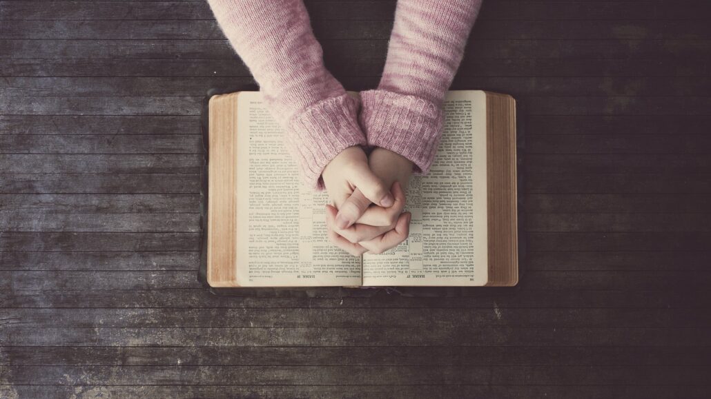 Hands folded together resting on a Bible