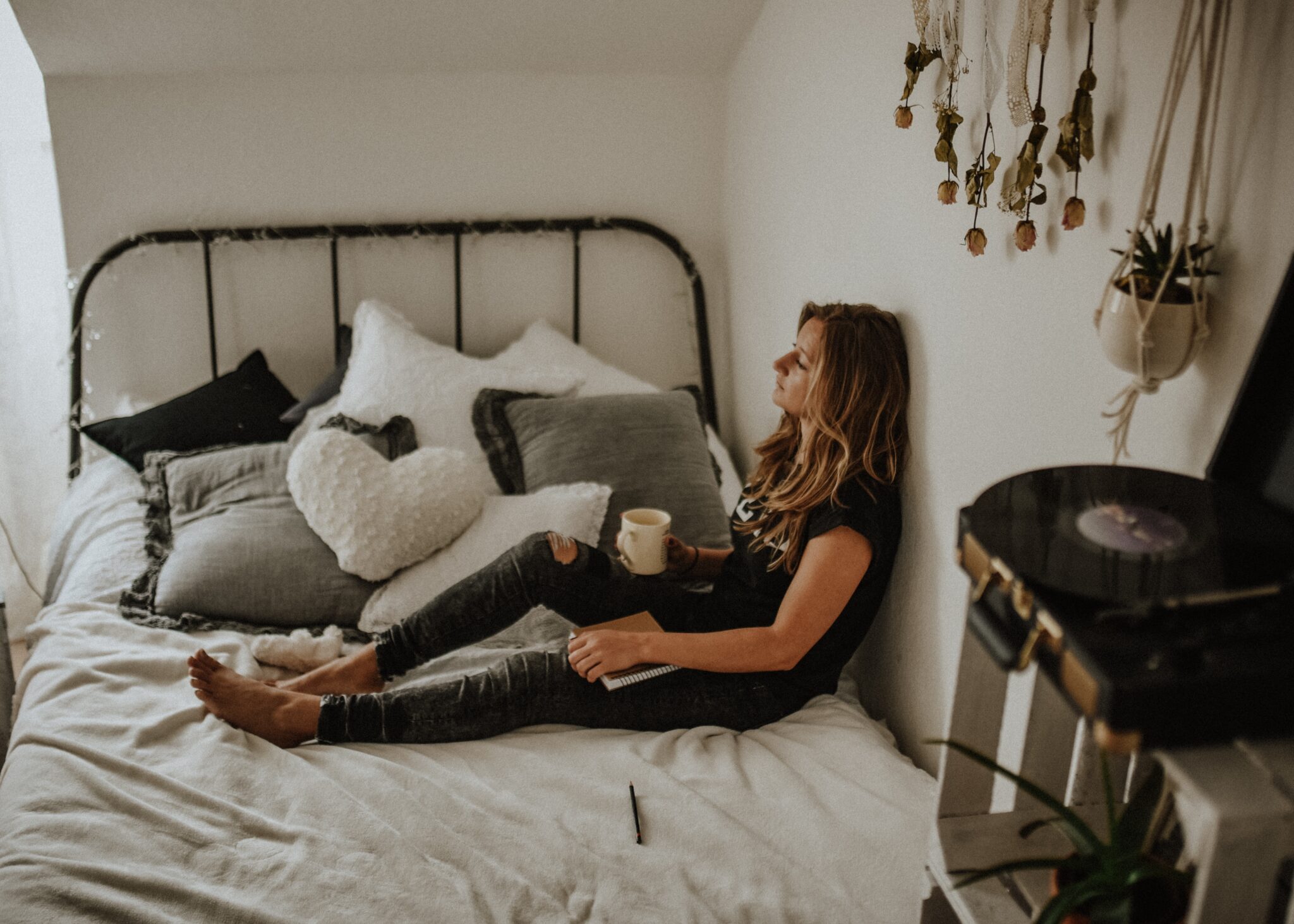 Person sitting with back against the wall on the bed holding coffee