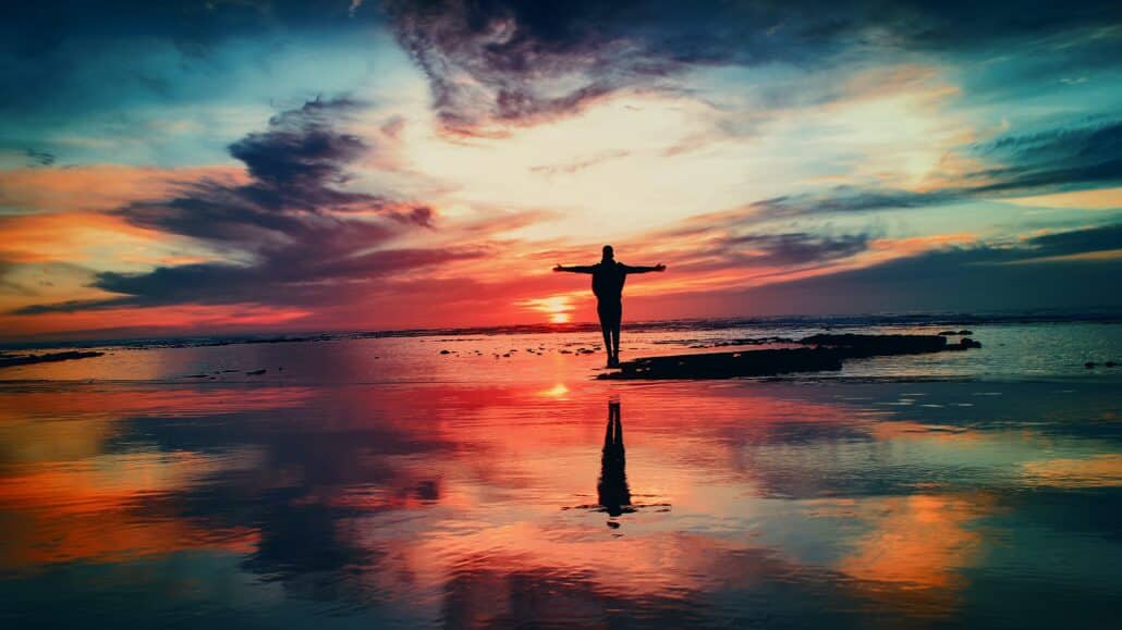 Person outstretches their arms at sunset on the beach