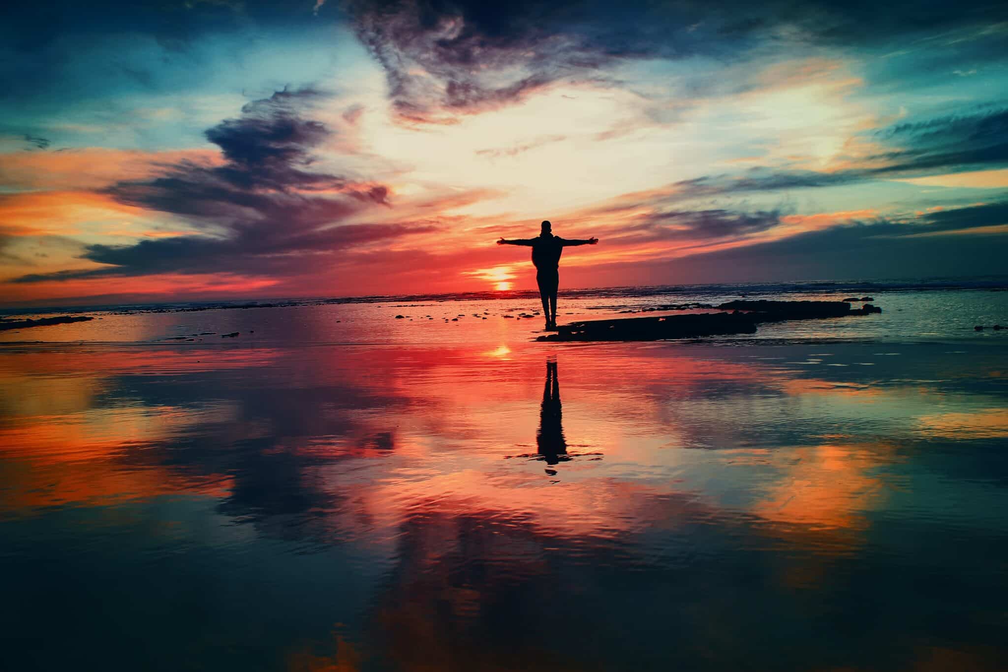 Person outstretches their arms at sunset on the beach