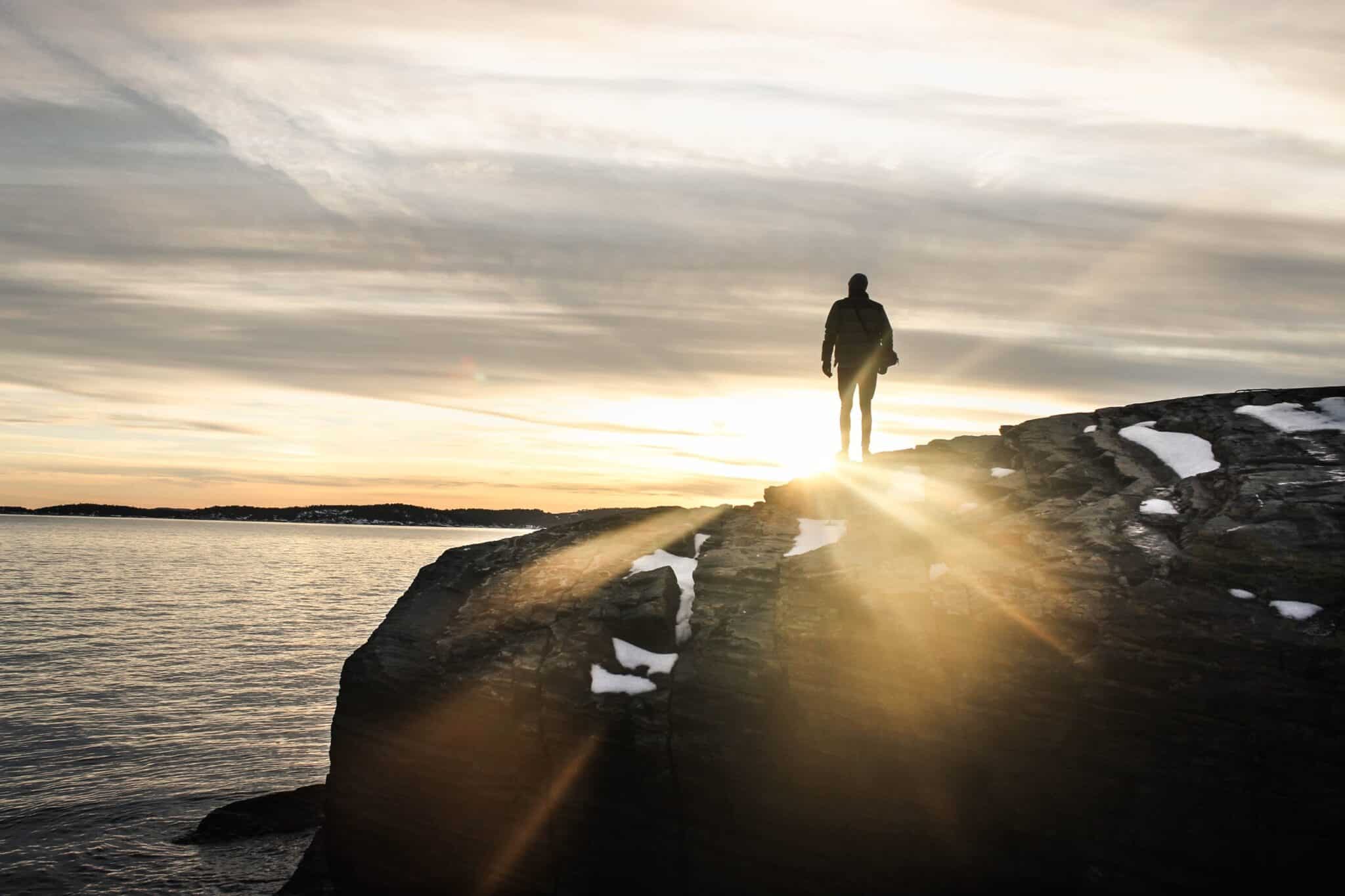 Person walking on a large rock next to a body of water