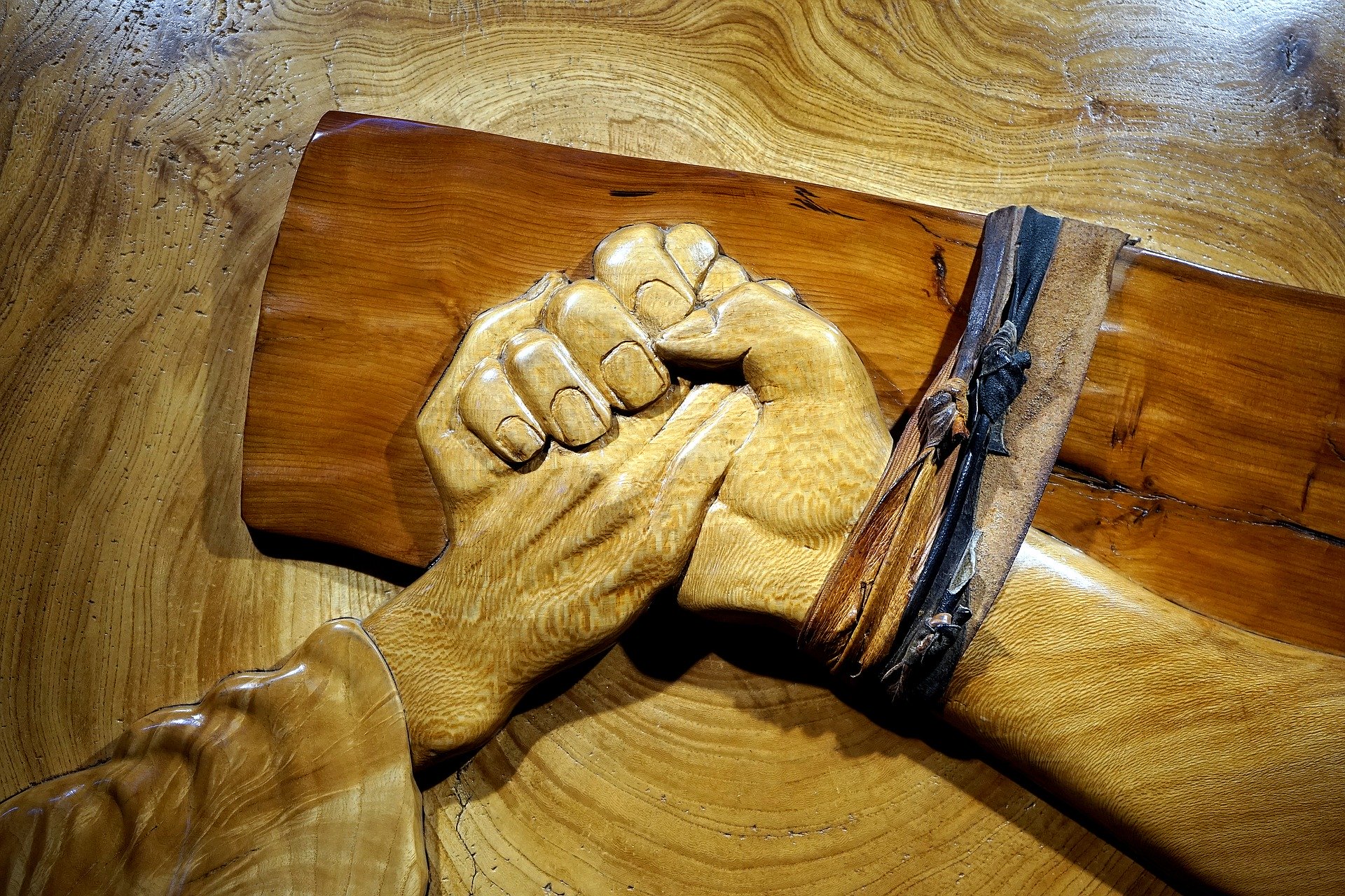 Wooden sculpture of a person holding Jesus' hand on the cross