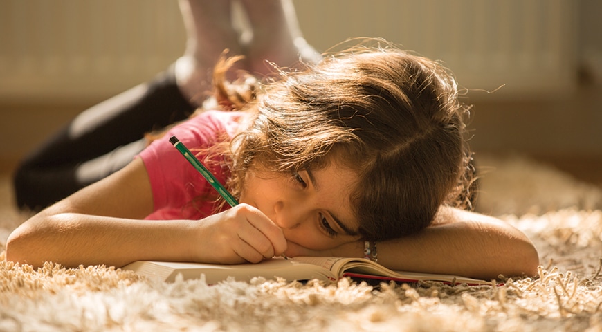 Young girl lying on the carpet and writing