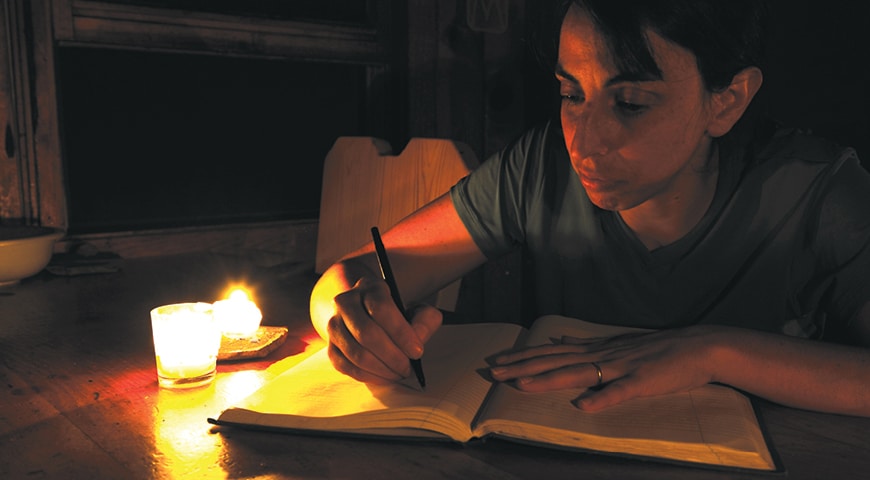 Person writing next to a lit candle