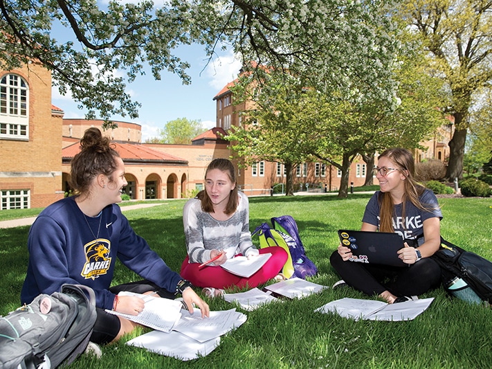 Three people studying in a patch of green grass