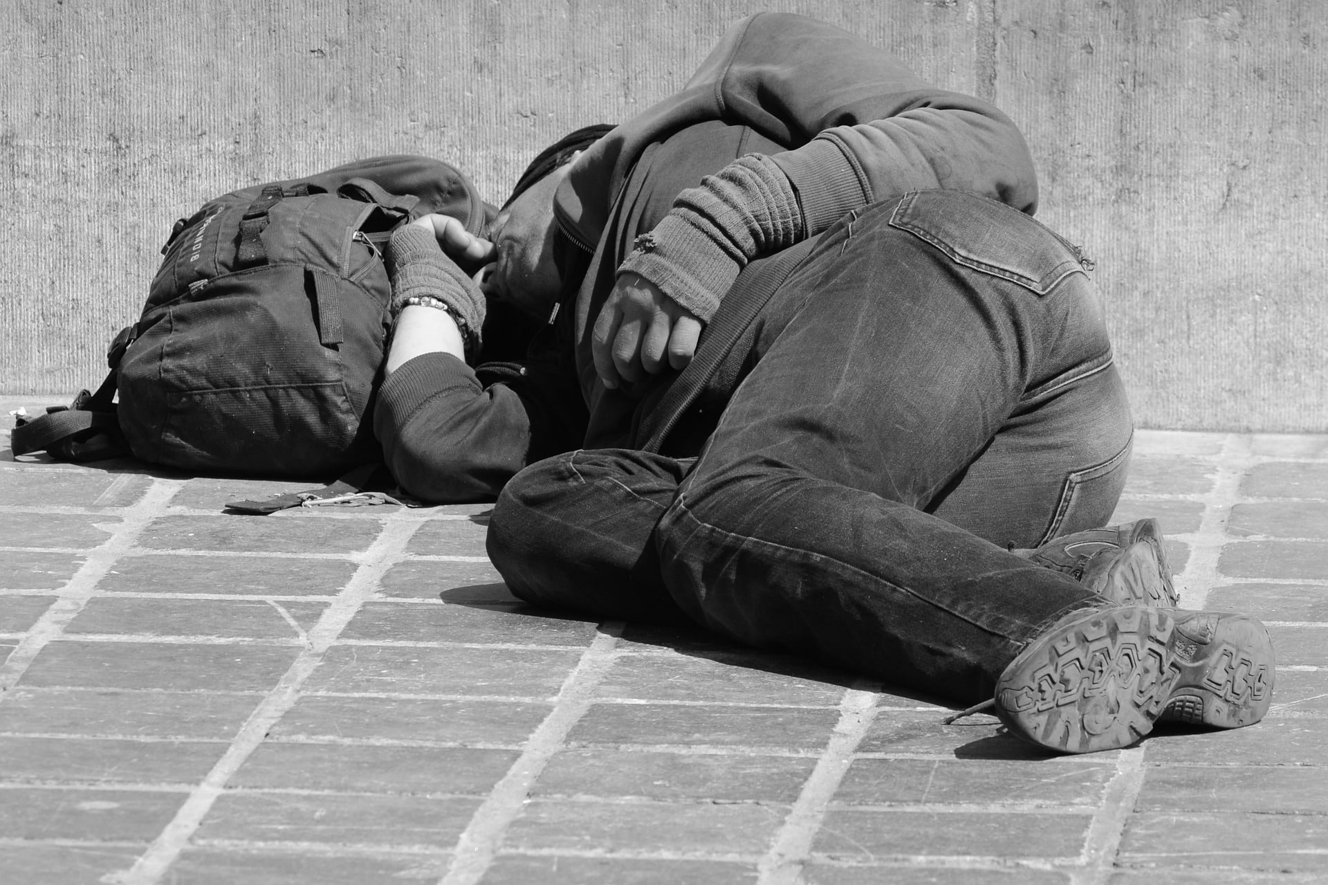 Homeless person sleeping next to a backpack