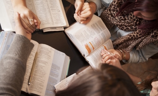 People holding hands around open Bibles