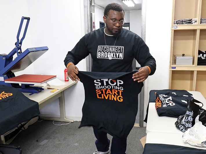 Person preparing shirts that say "Stop Shooting Start Living"