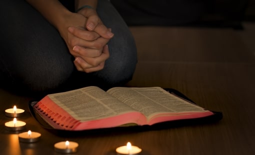 Person praying over an open Bible next to lit candles