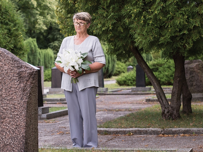 Person standing in front of a grave with flowers