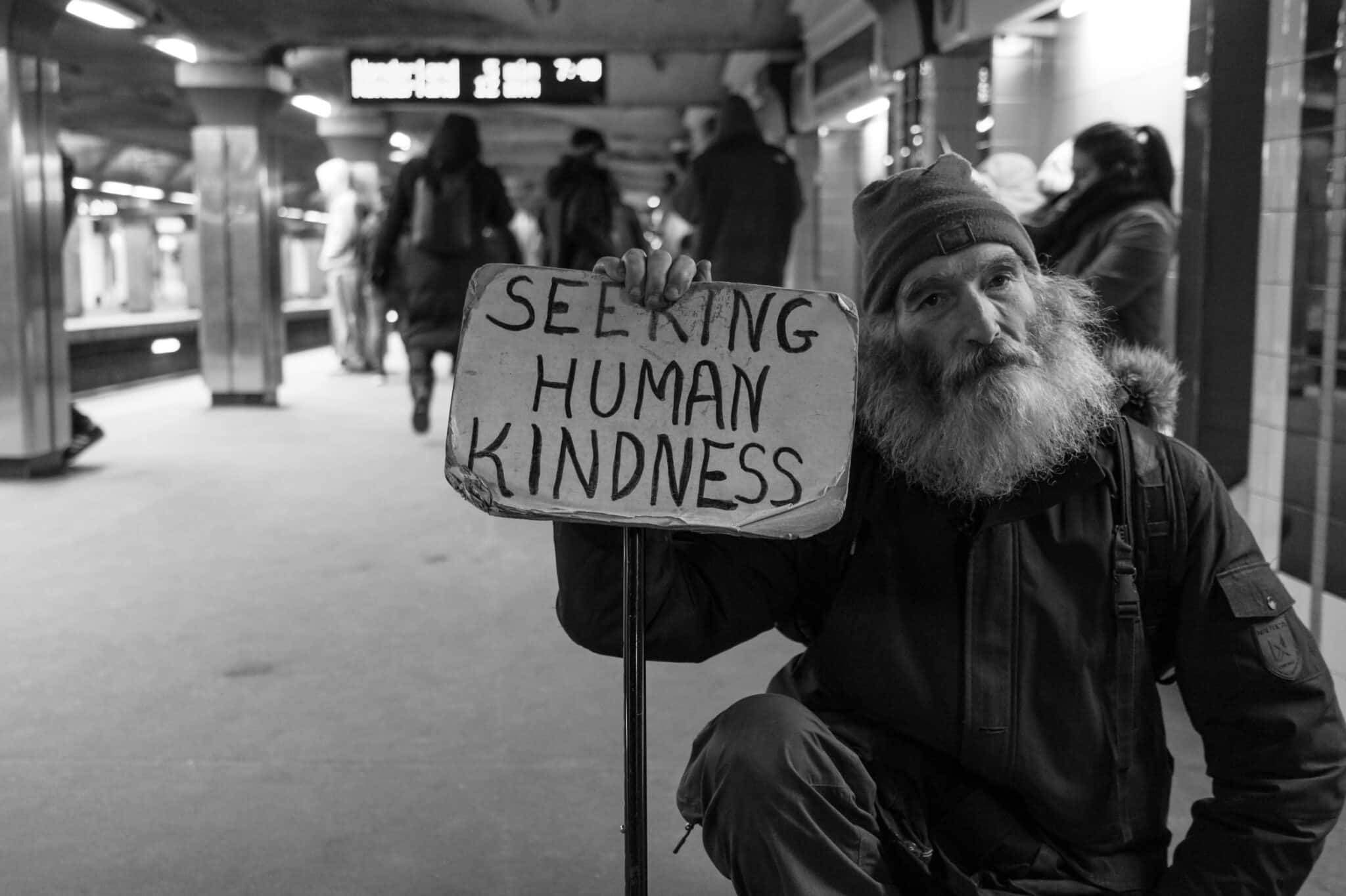 Person holding a sign that says "Seering Human Kindness"
