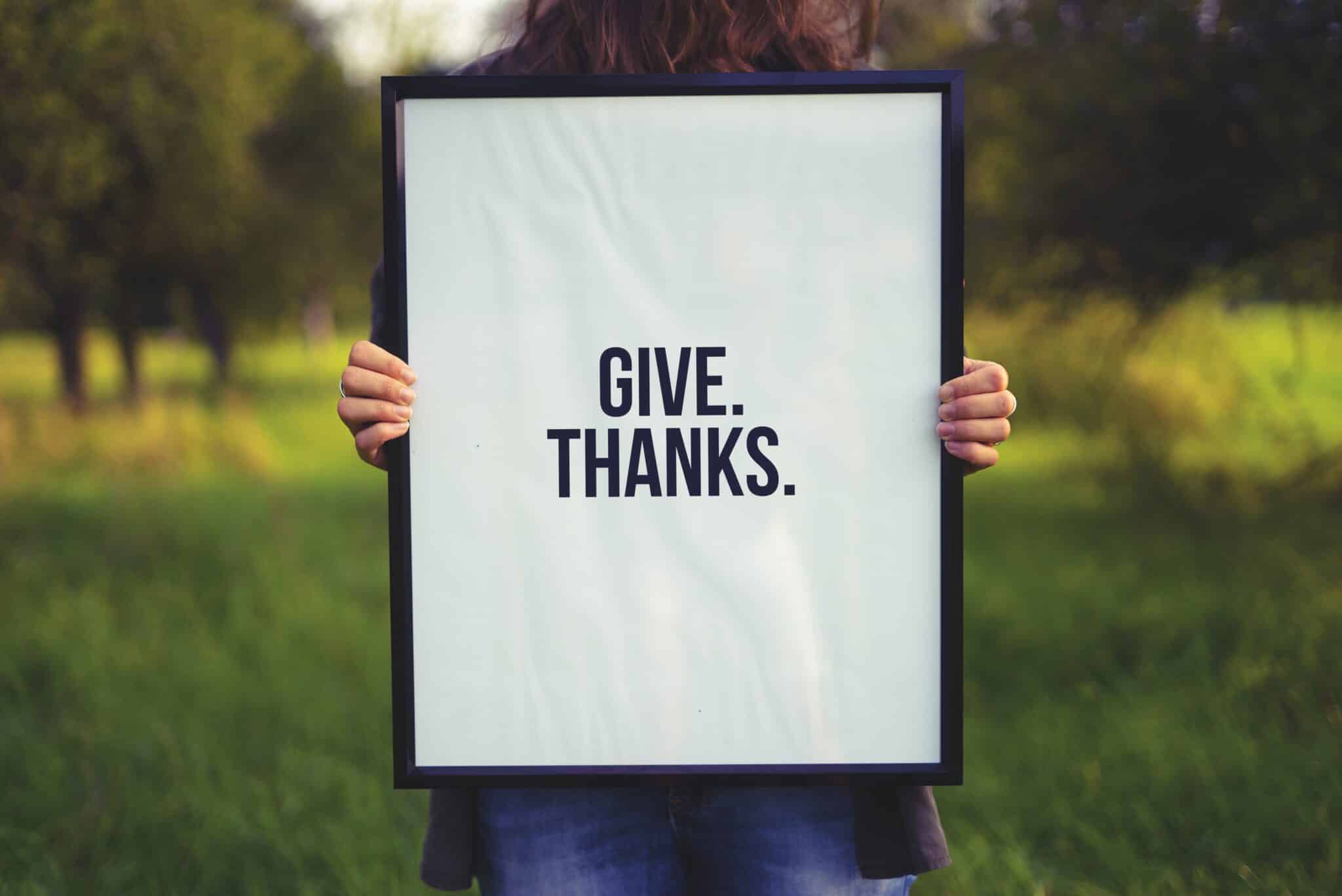 Person holding a sign that says "Give. Thanks."