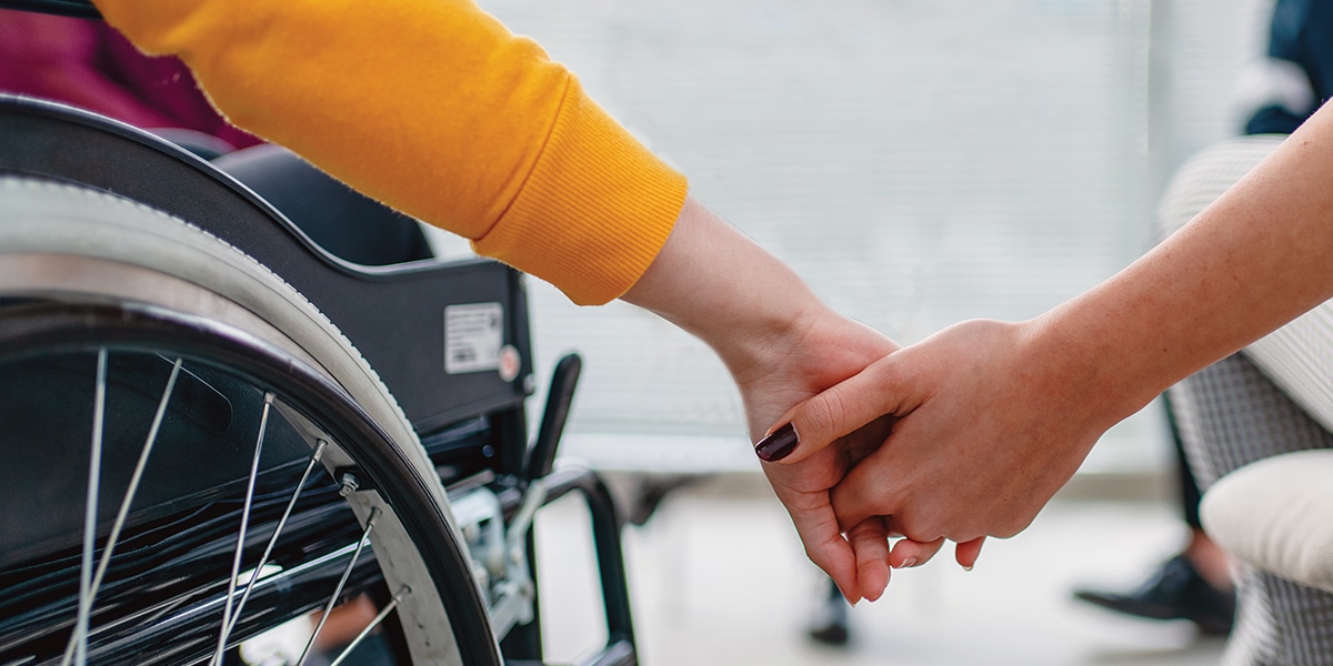 Person in chair and person in wheelchair holding hands