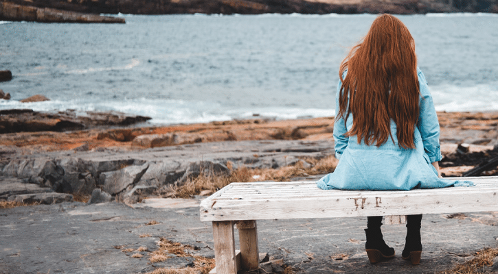 red haired woman on bench by the sea