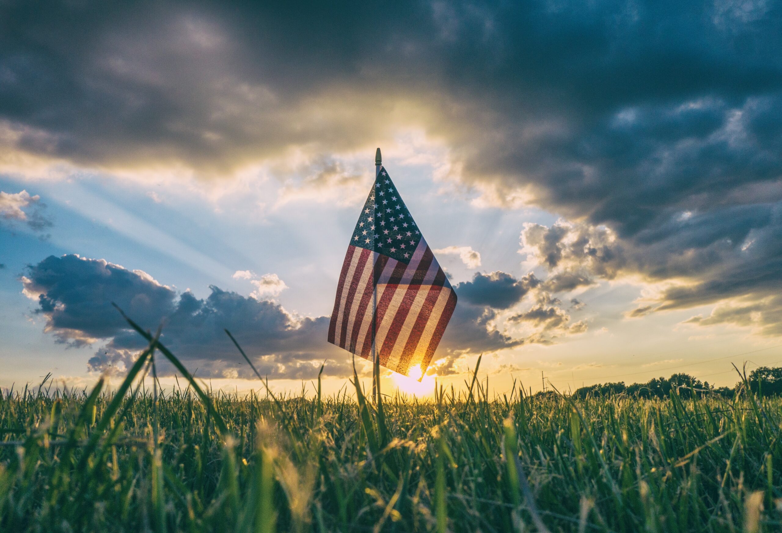 American flag with the sun behind it | Photo by Aaron Burden on Unsplash