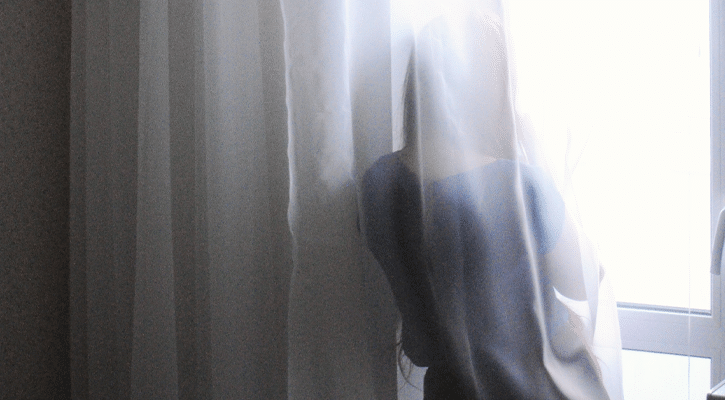 woman behind window curtain