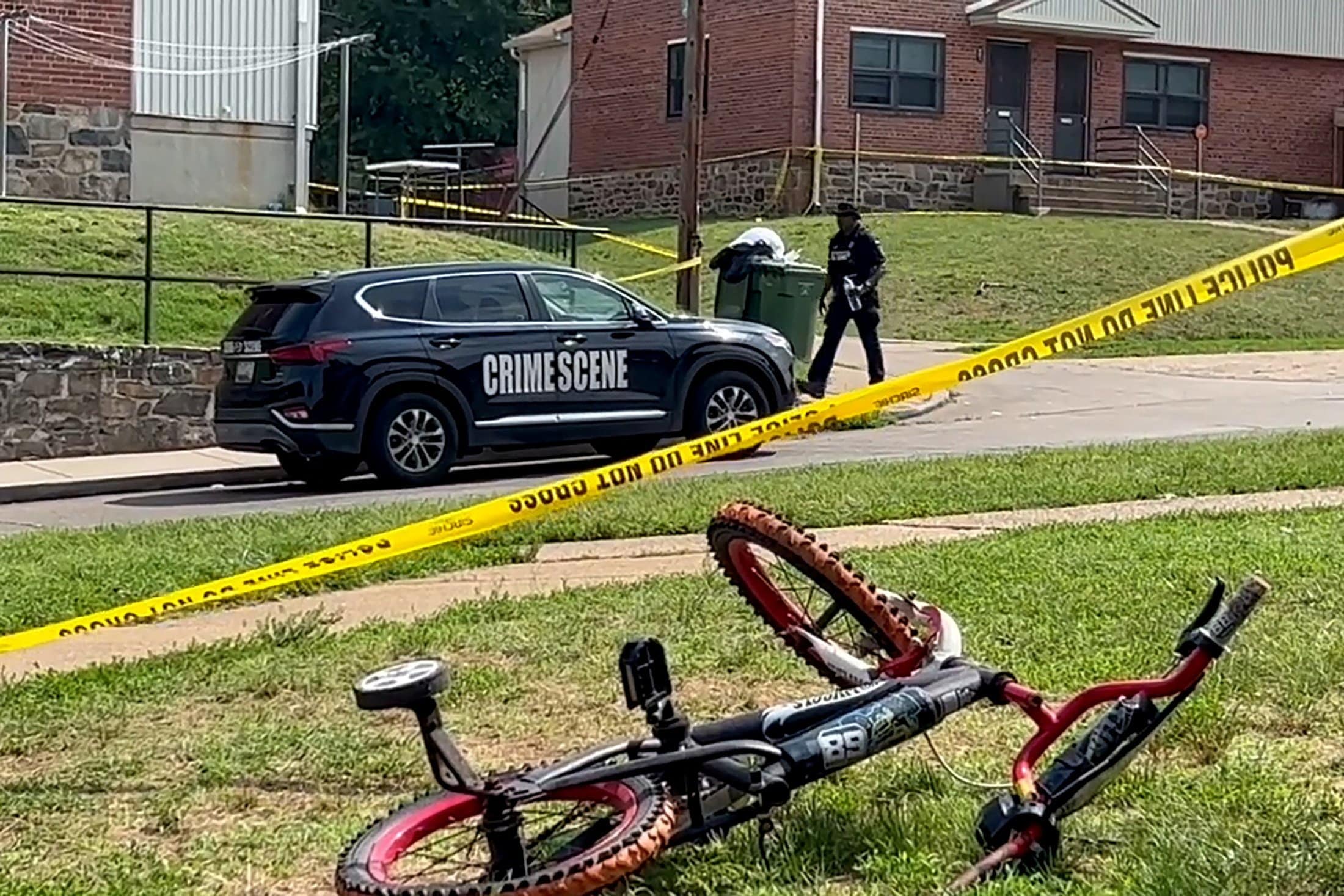 A child's bicycle, seen in a still image from video, lies on a lawn as a police office walks down a residential street in Baltimore July 2, 2023, after a mass shooting at a Fourth of July holiday weekend block party. Archbishop William E. Lori of Baltimore asked for prayers for the victims after the mass shooting left two dead and injured more than two dozen others, most of whom were teens. (OSV News photo/Reuters)