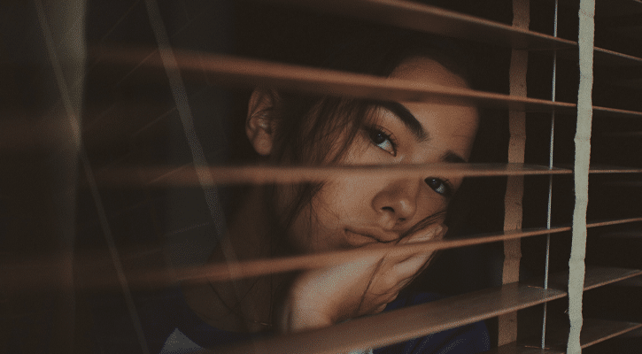 bored woman looking through wood blinds