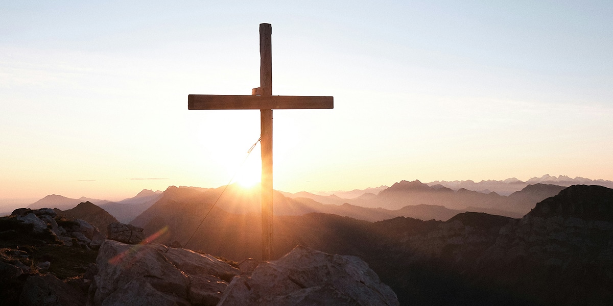 wooden cross on top of a mountain surrounded by mountains