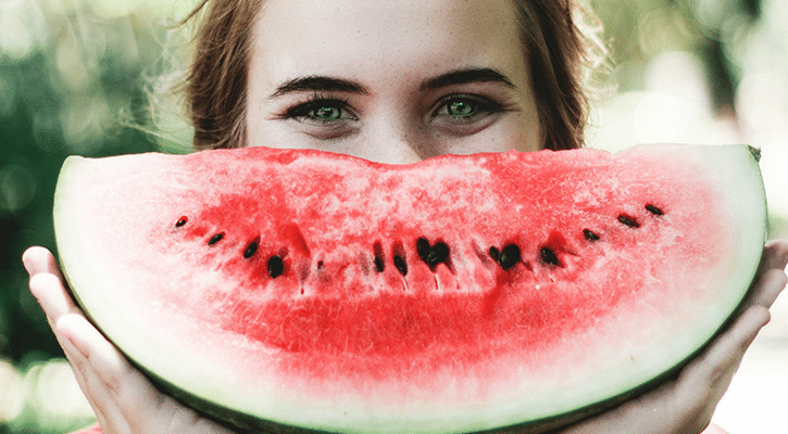 woman holding a watermelon in front of her face that looks like it is smiling