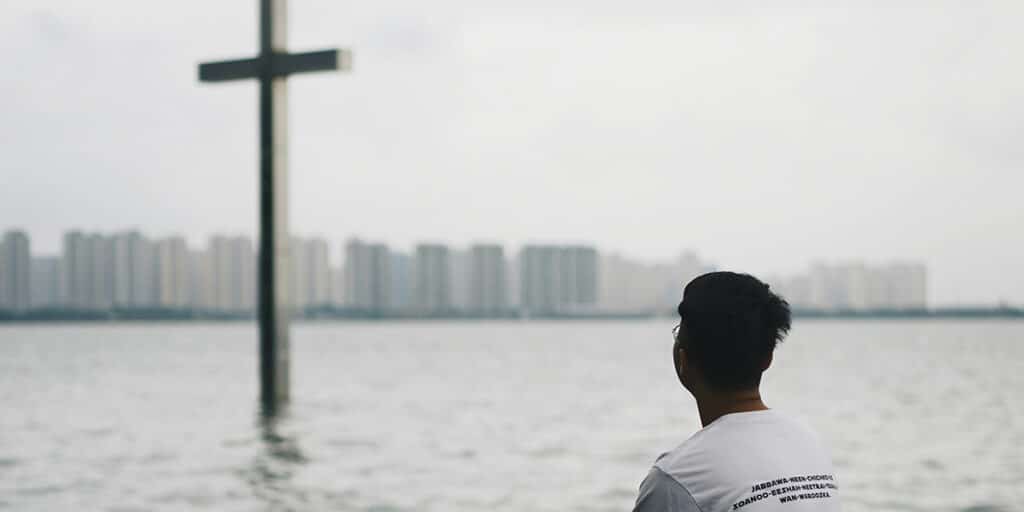 man looking at a cross in the water with a skyline in the background