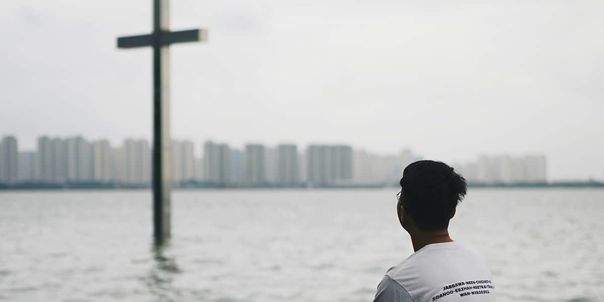 man looking at a cross in the water with a skyline in the background