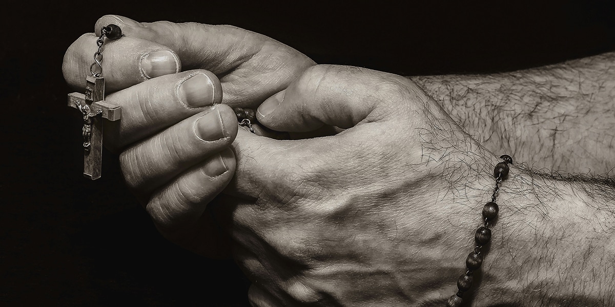 man's hand holding a rosary while praying