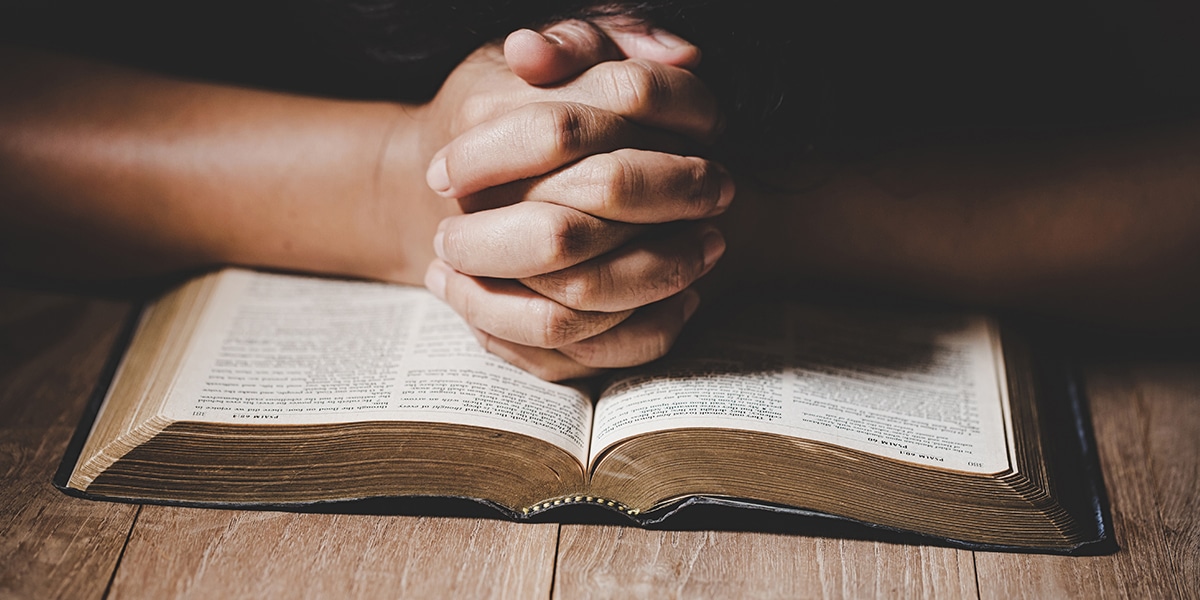 hands folded in prayer on top of a Bible