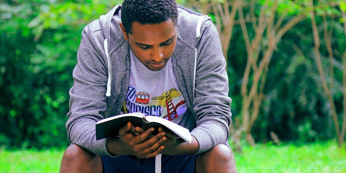 young man sitting outside and reading Bible