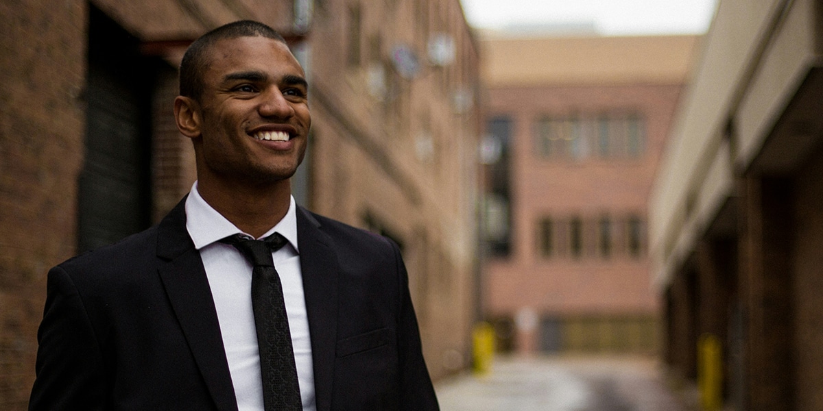 man smiling, wearing a suite and tie on the street.