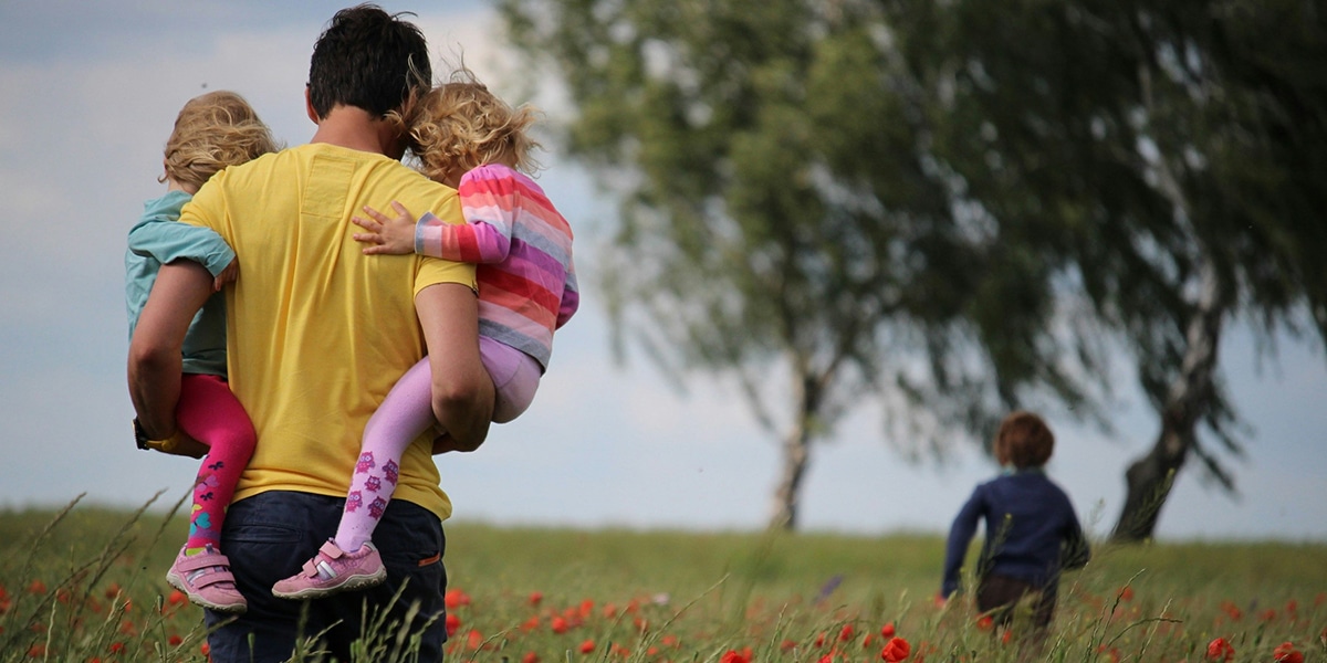 man carrying two kids on his arms.