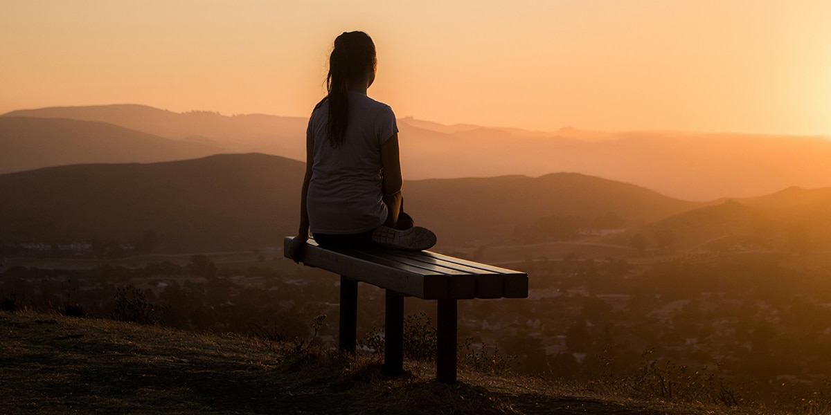 woman sitting quietly on a bench at sunset