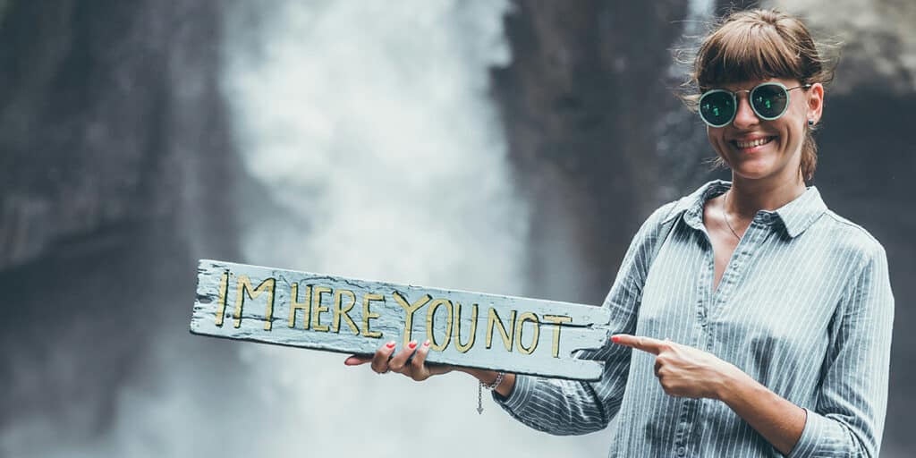 woman holding sign "I'm here you not" sign at a waterfall