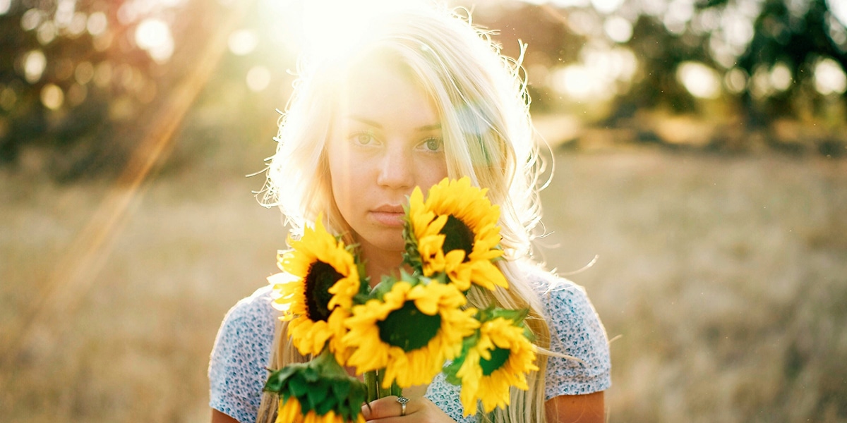 Young woman holding sunflowers in her hands while standing in a field