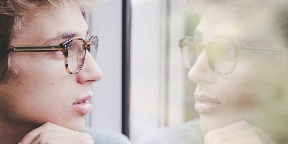 A young man's face reflecting in a window