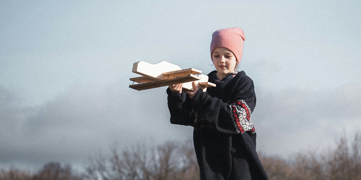 girl running through a field with a wooden toy airplane