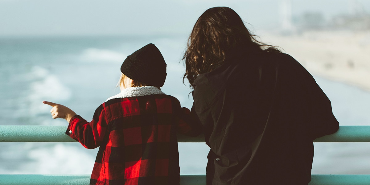 mother watching over her child while standing at a peer at the ocean.