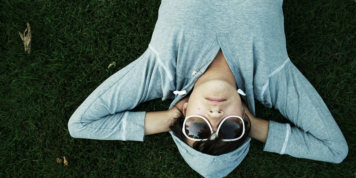 person with sunglasses laying on grass resting