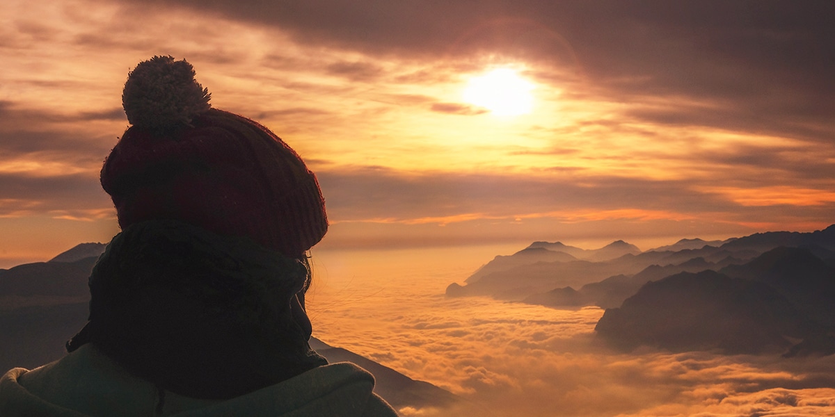 person watching sunset over cloudy mountains