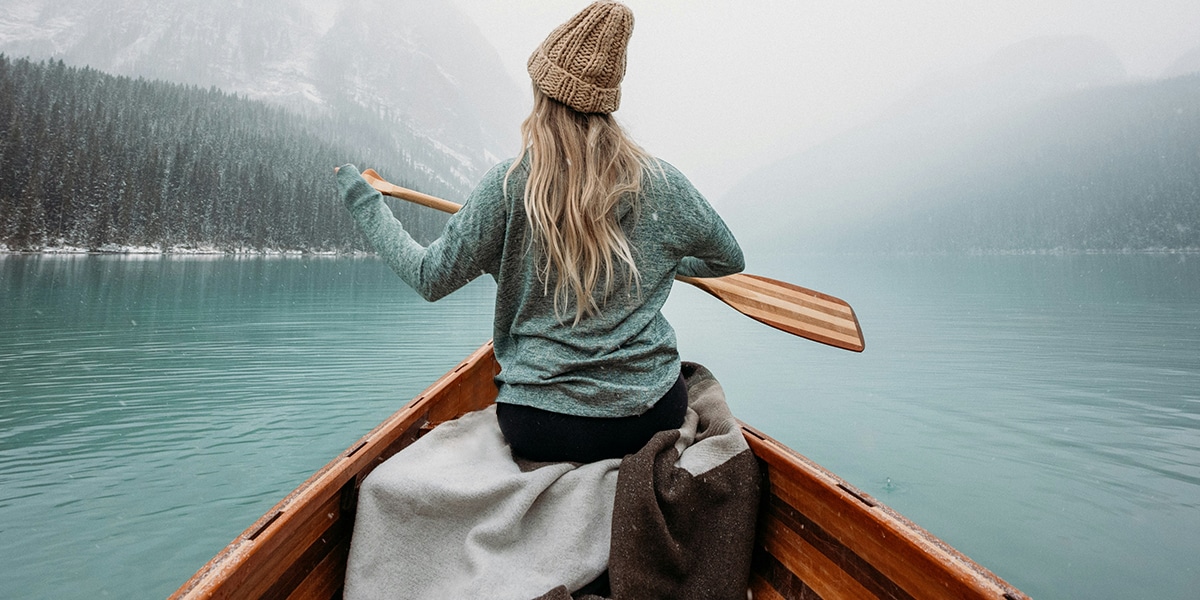 woman in a boat surrounded by water, forest and fog
