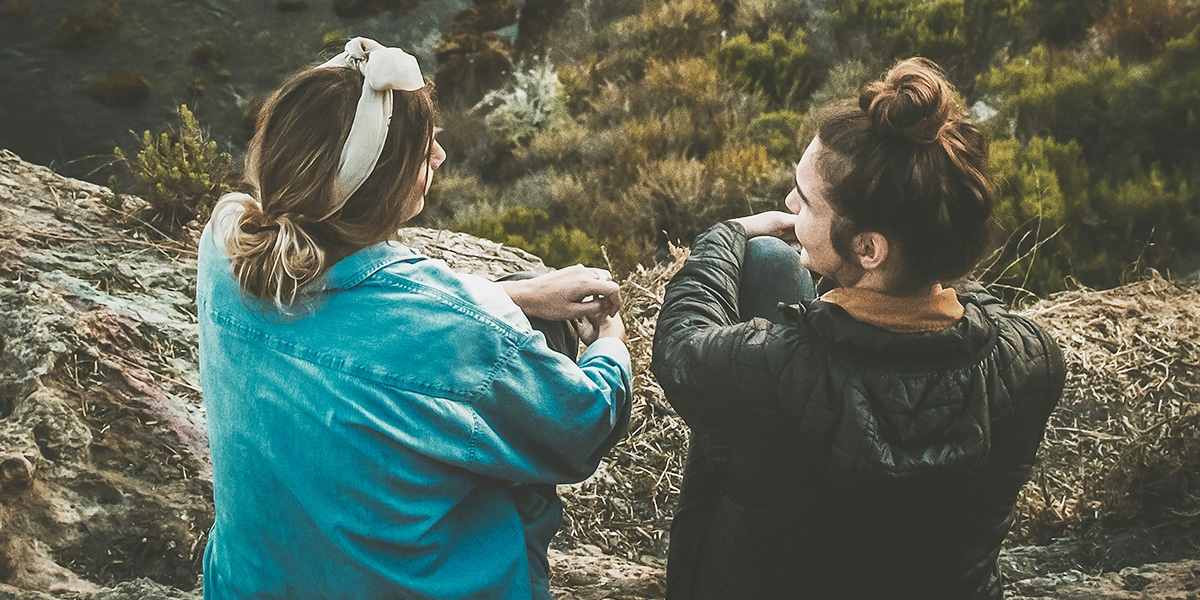 two women sitting on a hill, having a conversation