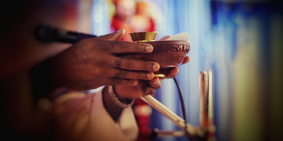 Priest's hands holding communion ware.