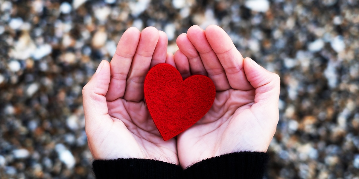 Open hands holding a red paper heart