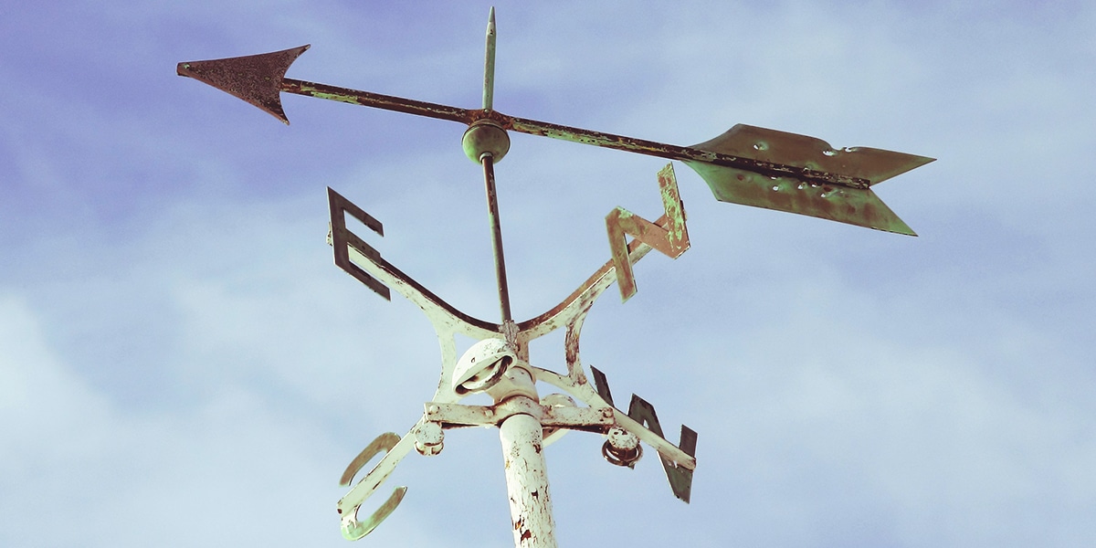 Wind vane with compass and arrow pointing in a direction.
